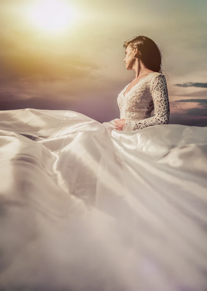 An editorial close-up of a bride's white floral lace gown in soft sunlight