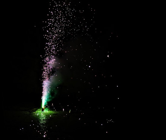 A vibrant burst of neon green fireworks exploding against a black sky with sparks flying.