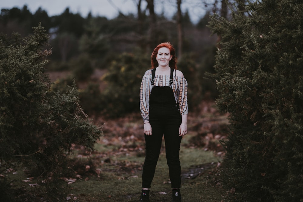 woman in black dungarees standing beside trees