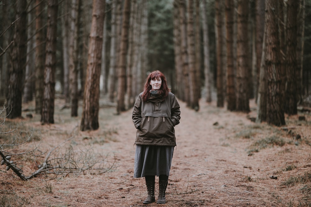 woman in green jacket standing in the middle of dirt trail at the woods