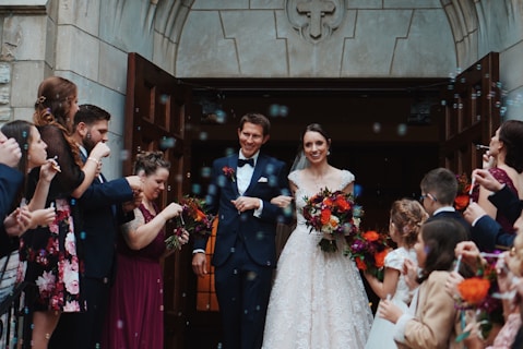 groom and bride standing between the crowd near building during daytime