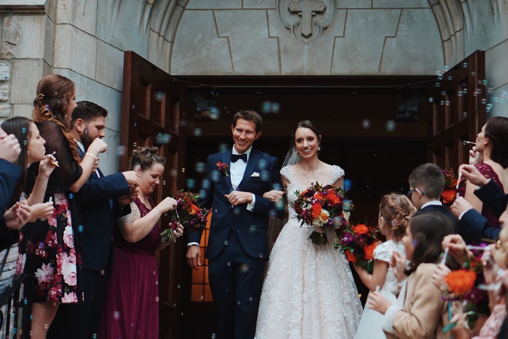 Le marié et la mariée se tiennent au milieu de la foule près du bâtiment pendant la journée