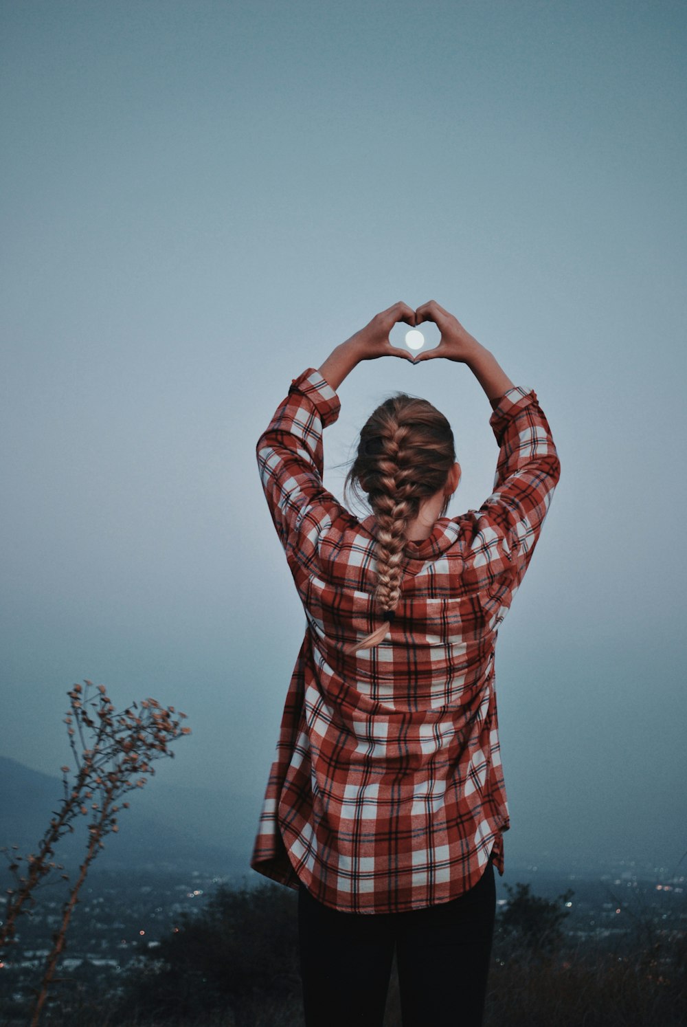 woman wearing red, white, and black plaid dress shirt raising hand doing heart shape hand