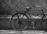 A black and white photo of an old bicycle leaning against a brick wall.