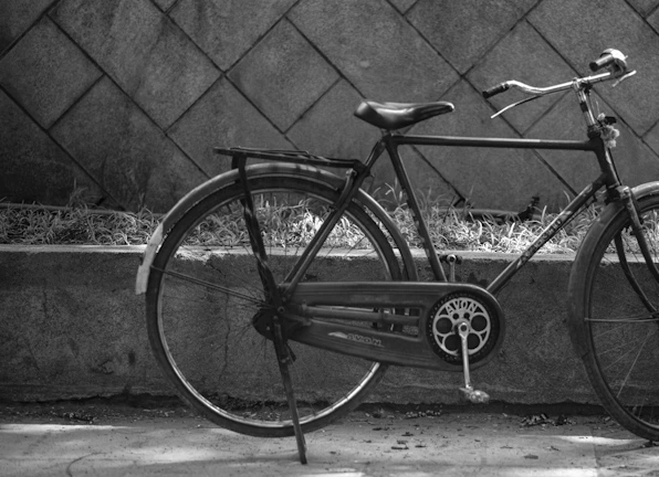 A black and white photo of an old bicycle leaning against a brick wall.