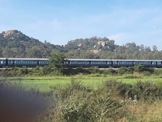 A scenic train winding through lush green hills under a clear blue sky.