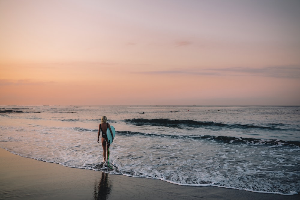 woman carrying surfboard walking on beach