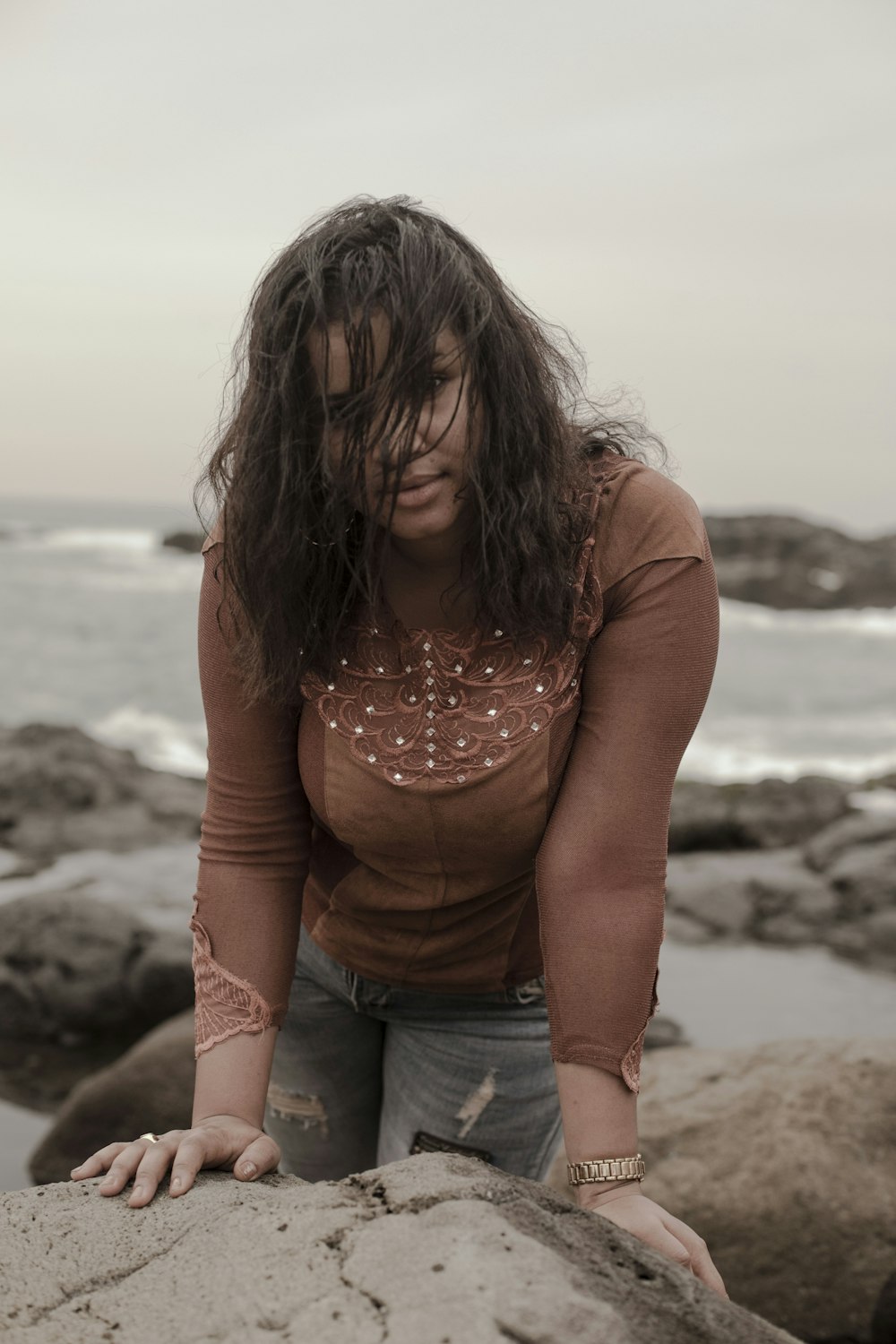 woman in brown long sleeved shirt leaning on stones