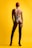 A person with red hair is wearing a strappy one-piece swimsuit and high black heeled boots, standing against a bright yellow background. The pose is from the back, with emphasis on the intricate design of the swimwear.