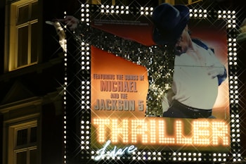 A large, illuminated sign featuring an iconic pose of a performer wearing a sequined jacket, white glove, and hat. The background is flavored with warm hues and the text highlights performance details, with prominent focus on 'Thriller Live' and associations with Michael and the Jackson 5.