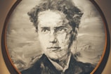 A monochromatic portrait painting of a person with a focused and serious expression. The brush strokes are bold, creating a texture that gives the image a sense of movement and depth. The artwork is enclosed within a circular frame.