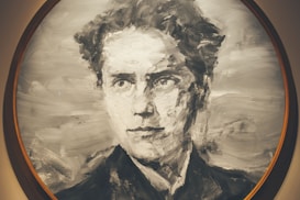 A monochromatic portrait painting of a person with a focused and serious expression. The brush strokes are bold, creating a texture that gives the image a sense of movement and depth. The artwork is enclosed within a circular frame.