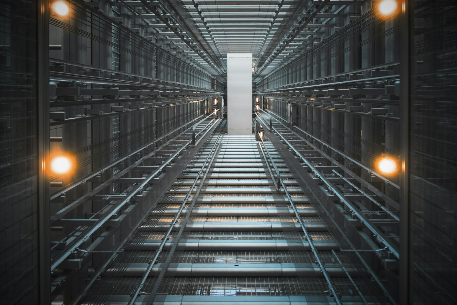 Looking up a lit elevator hoistway at the guide rails, counterweight, and structural steel framing