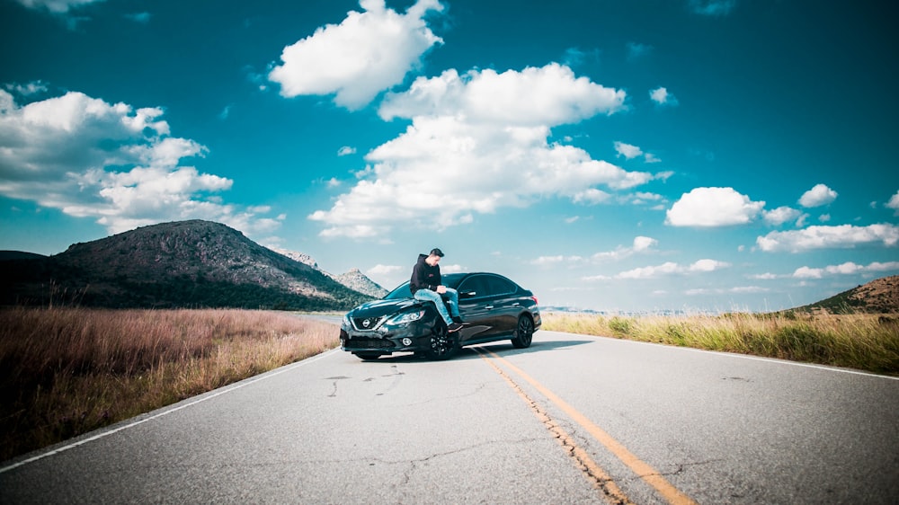 man sitting on front of vehicle hood on road during daytime