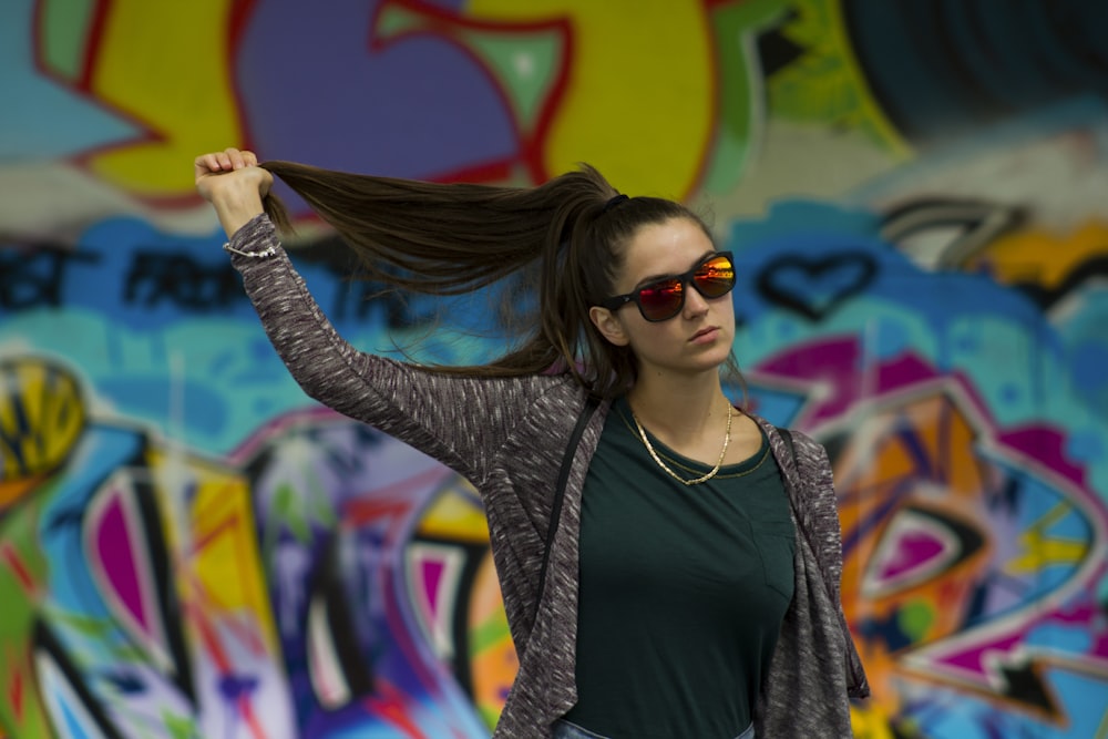 Frau, die ihr Haar hält, steht in der Nähe einer Graffiti-Wand