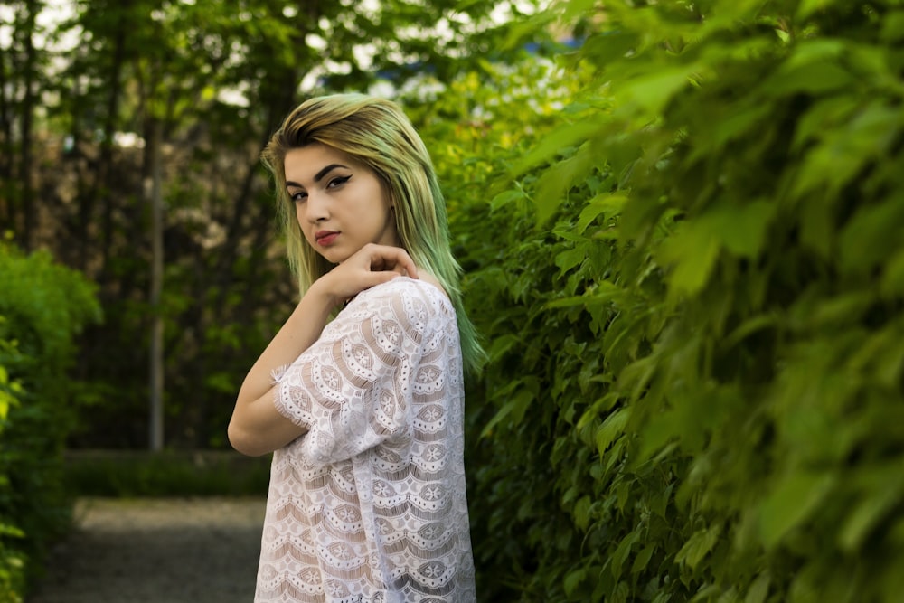 woman in white lace top standing beside green-leaf plant during daytime