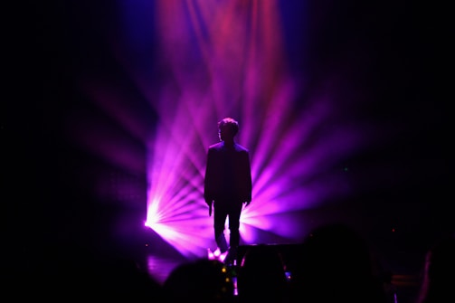 A dimly lit stage with Binaira Mai silhouetted against deep blue and purple lights, embodying strength and authenticity.