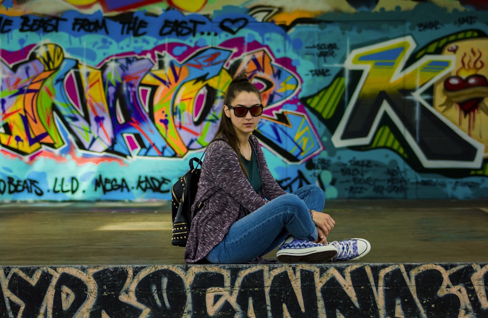 woman sitting on stage beside graffiti