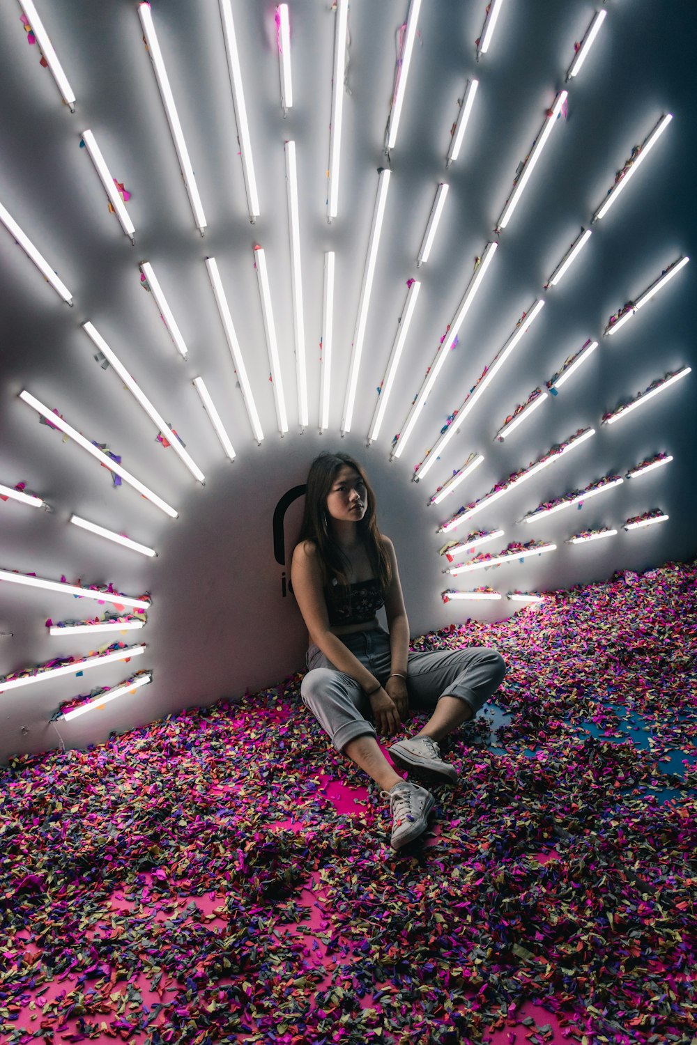 woman sitting on floor with pink petals and fluorescent lights on the wall\
