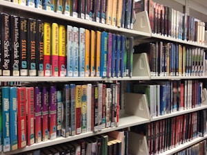 Rows of colorful books neatly arranged on white library shelves. The spines display various titles and authors, reflecting diverse genres. The arrangement suggests organization and accessibility for readers.