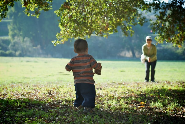 An earthly protector helping a child across a cobblestone path under soft sunlight.