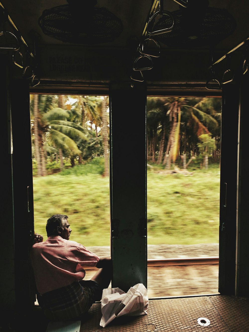Mann sitzt auf Türschwelle in der Nähe von Kokospalmen