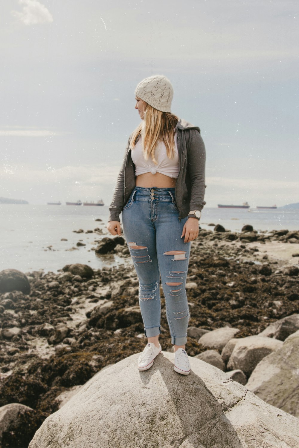 woman standing on boulder overlooking ocean during daytime