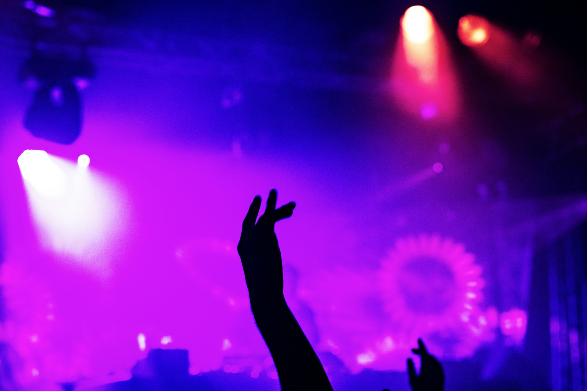 Close-up of hands raised in the air, illuminated by pulsating neon lights, capturing the energy of an underground psy-trance event.