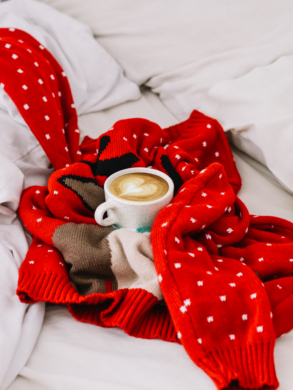 Taza redonda de cerámica blanca con bebida de café en el interior sobre suéter de punto de lunares rojos y blancos