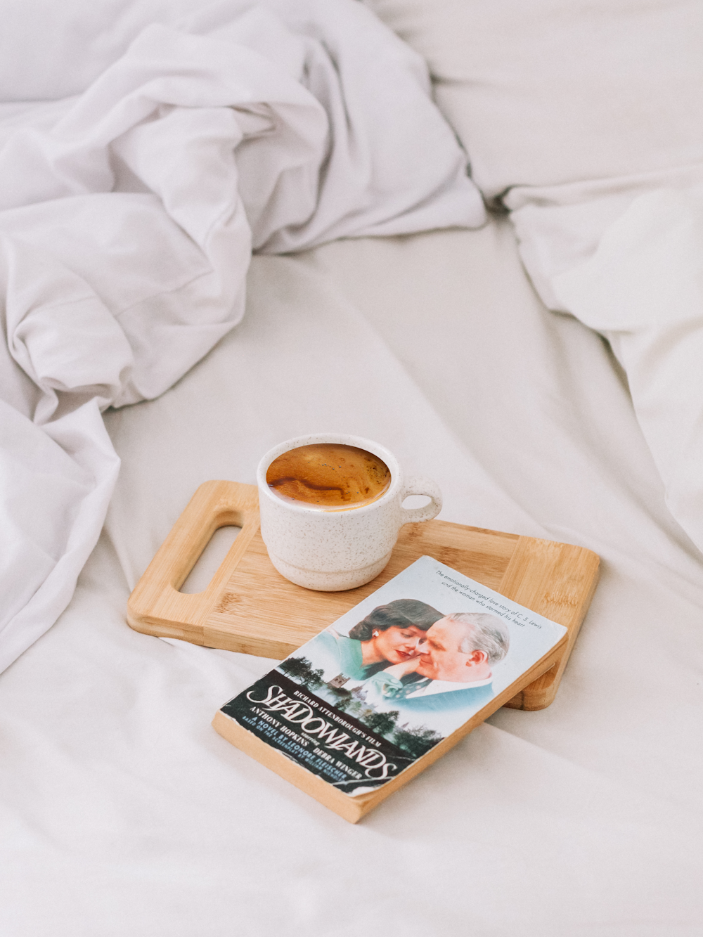 white ceramic mug with coffee on brown wooden serving tray and book