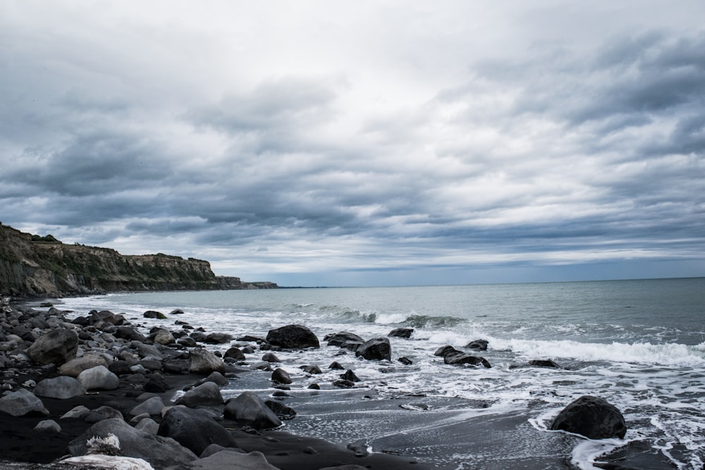 seashore beside rocks under white and gray clouds