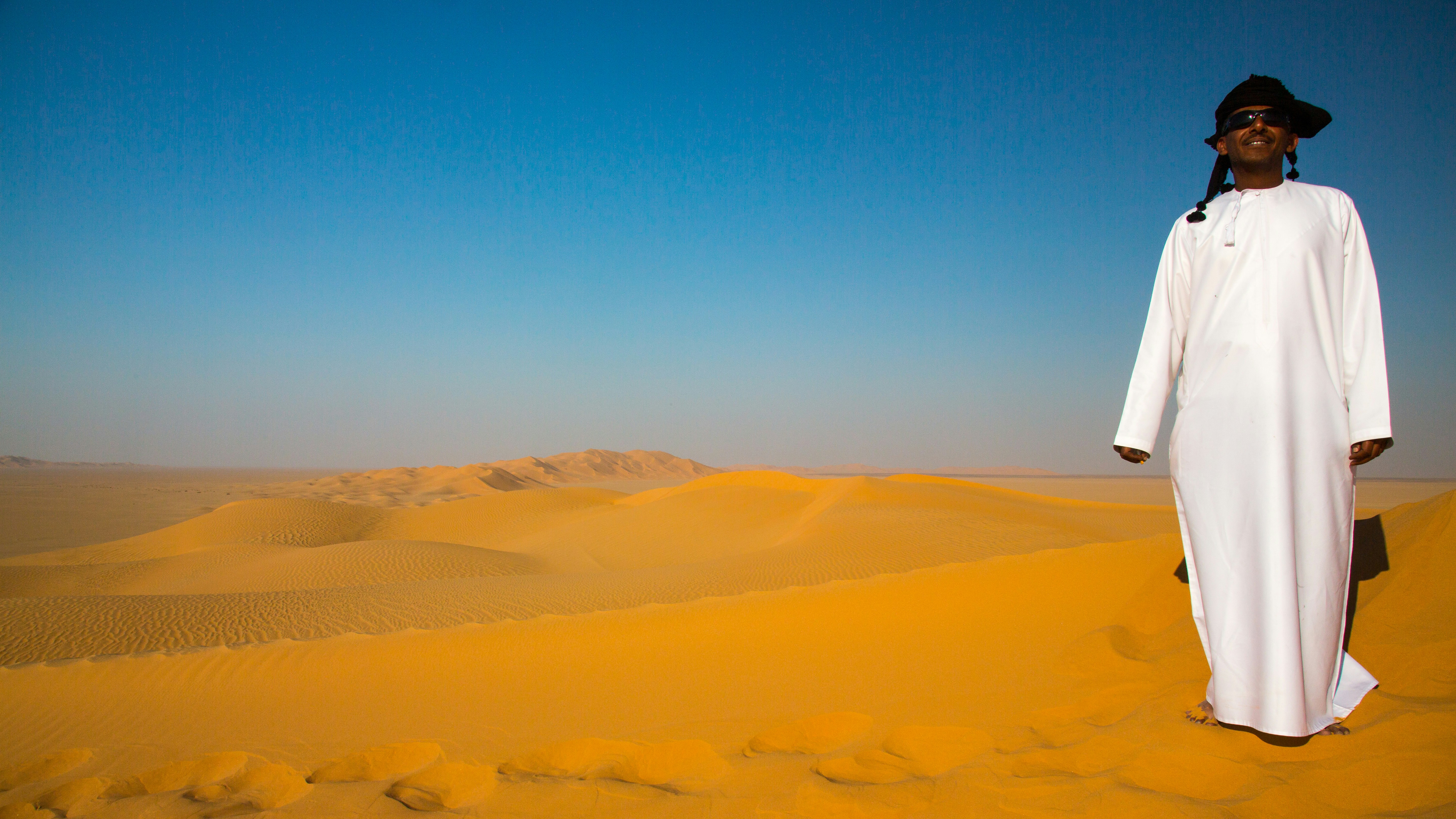 Man in traditional Emirati thobe walking across desert dunes