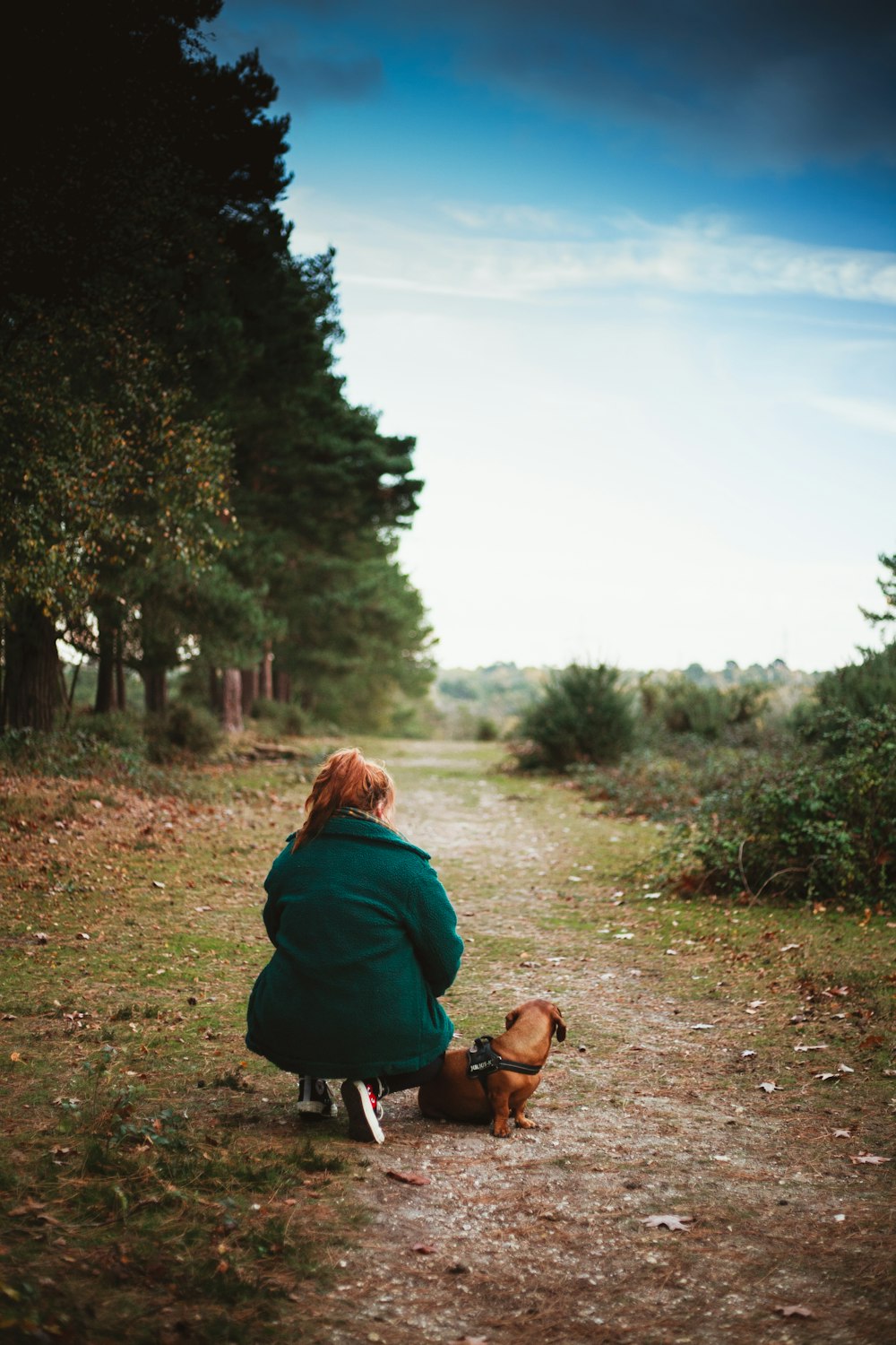 woman squatting beside dog on ground near trees