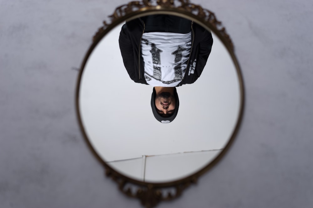 round brass-colored framed mirror with reflection of man