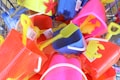 A collection of brightly colored plastic beach toys, including shovels, buckets, and crab and starfish molds, all wrapped in netting. The toys are in shades of yellow, red, blue, and pink, and appear to be packed in a basket or display.