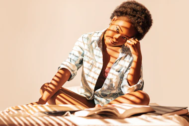 A girl sitting cross-legged on a bed reading in warm afternoon light.