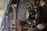 A close-up view of a large, industrial wheel hub attached to a vehicle axle. The image shows intricate mechanical details, including heavy bolts, a metallic hub cap with embossed text, and weathered metal surfaces, suggesting a focus on robust engineering and machinery.