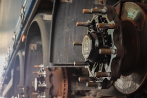 A close-up view of a large, industrial wheel hub attached to a vehicle axle. The image shows intricate mechanical details, including heavy bolts, a metallic hub cap with embossed text, and weathered metal surfaces, suggesting a focus on robust engineering and machinery.
