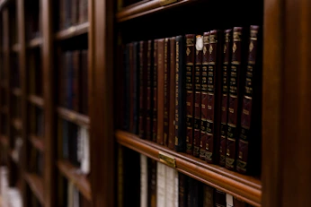 A close-up of aged law books stacked on a dark wooden shelf under warm light.
