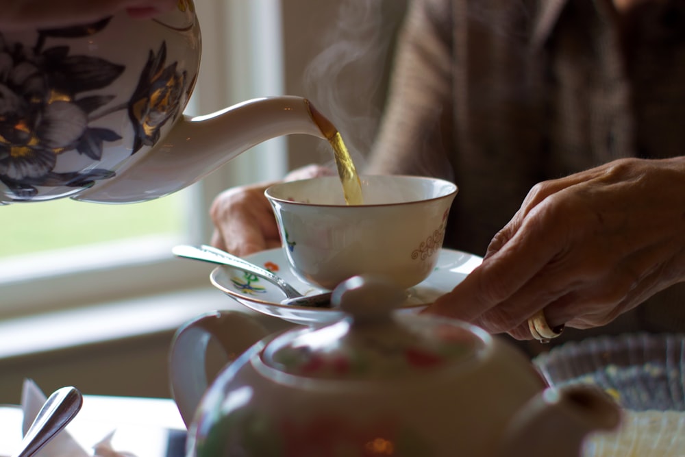 white ceramic teapot pouring tea on cup
