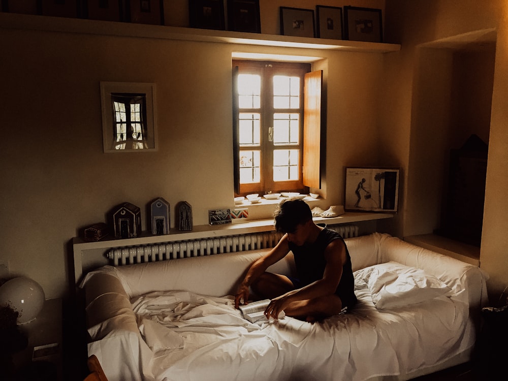 man sitting on bed beside opened window