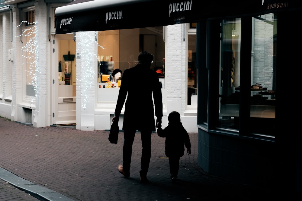 silhouette photography of man and child walking beside building
