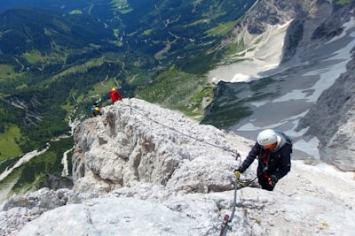 three people climbing on rock mountain during daytime dangerous teams background