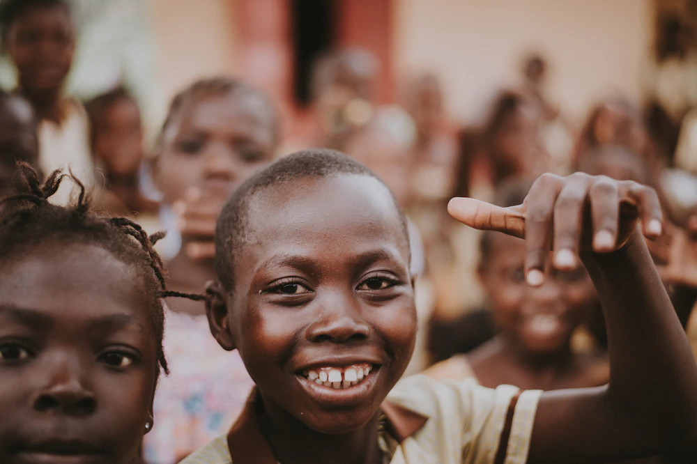 A community volunteer smiles while surrounded by a group of joyful children outdoors