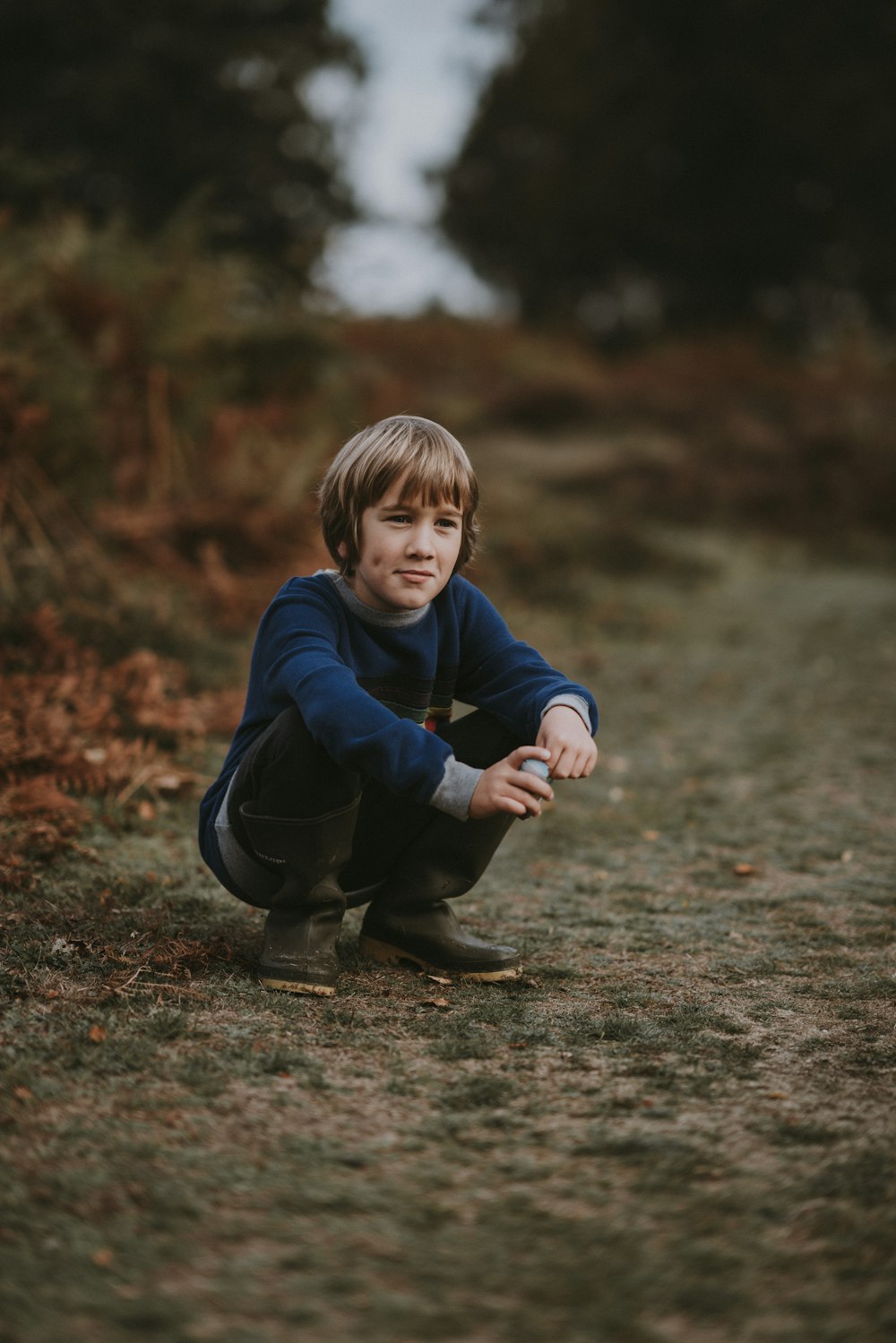 ragazzo in maglione blu accovacciato sul sentiero marrone