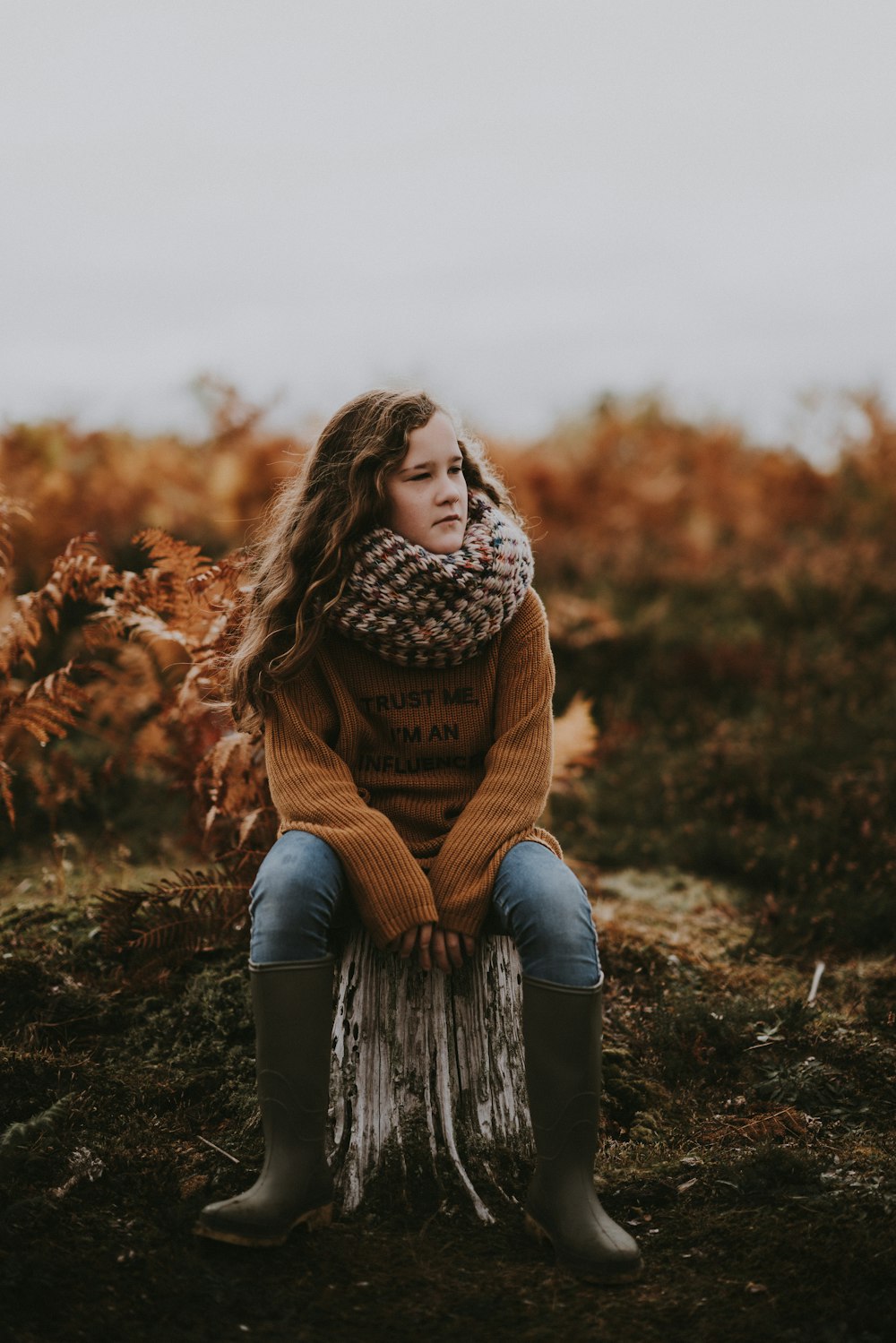 woman sitting on log under gray sky