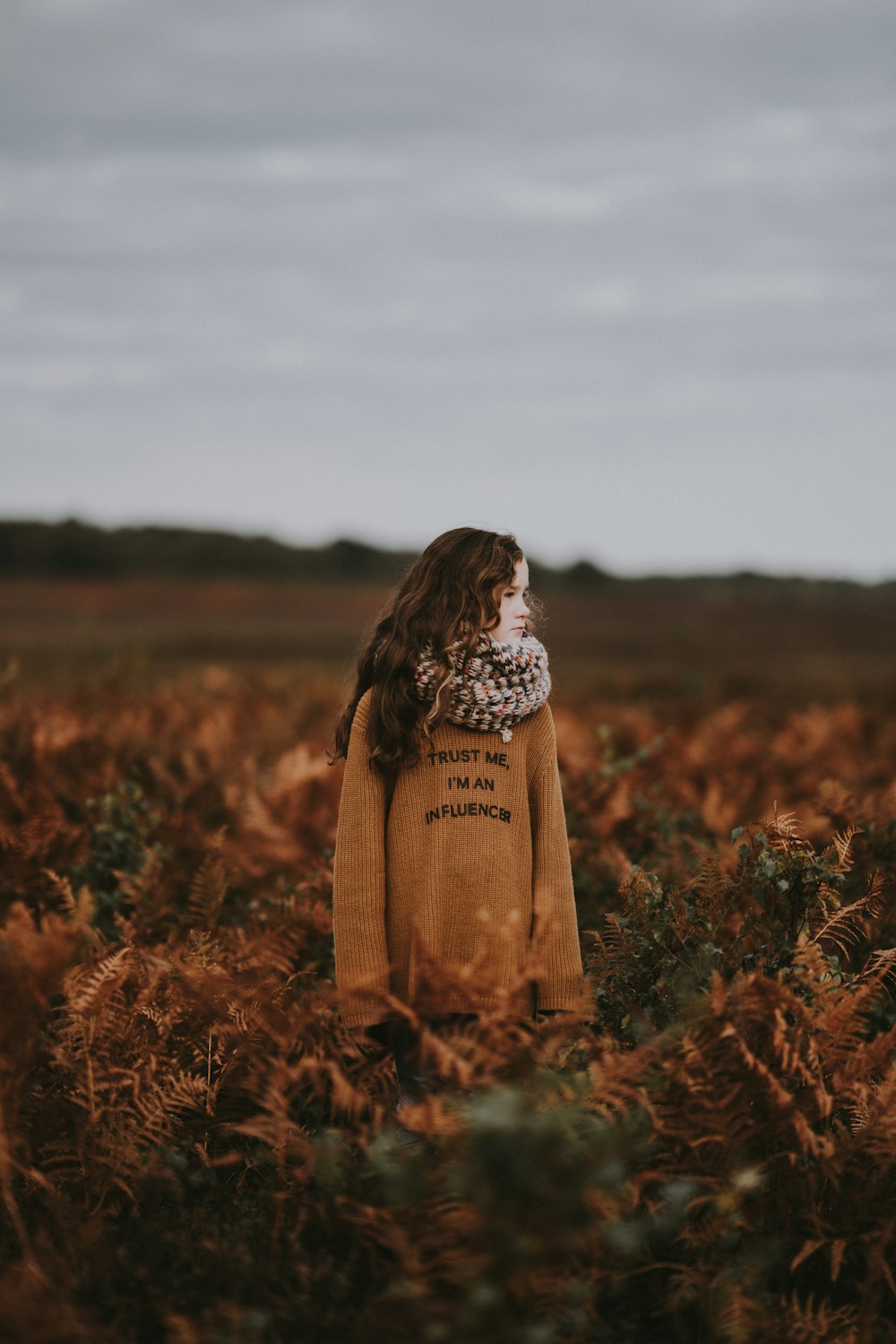 girl wearing brown jacket standing on brown field