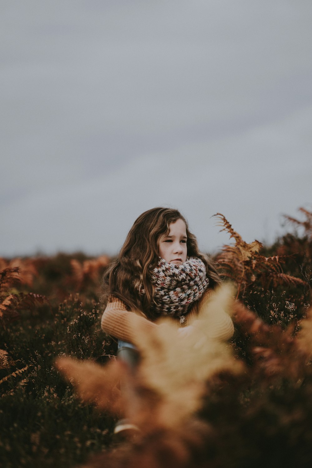 Photographie de mise au point sélective d’une fille portant une écharpe debout entourée de plantes