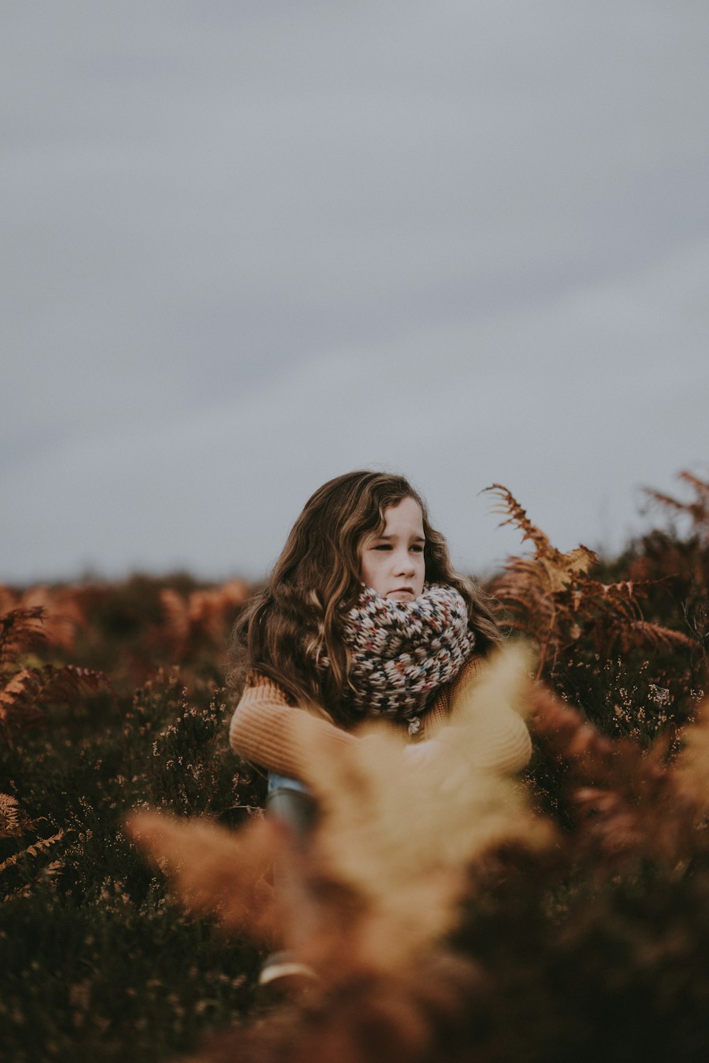 selective focus photography of girl wearing scarf standing surrounded by plants