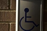 A metal sign with a blue symbol of a person in a wheelchair, mounted on a brick wall.